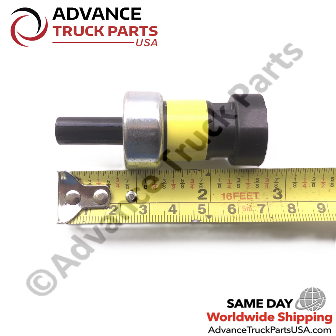 Advance Truck Parts USA pressure switch showing a horizontal profile displayed above a measuring tape highlighting the black pneumatic tube, metallic center body, yellow identification band, and black electrical connector on a plain white background