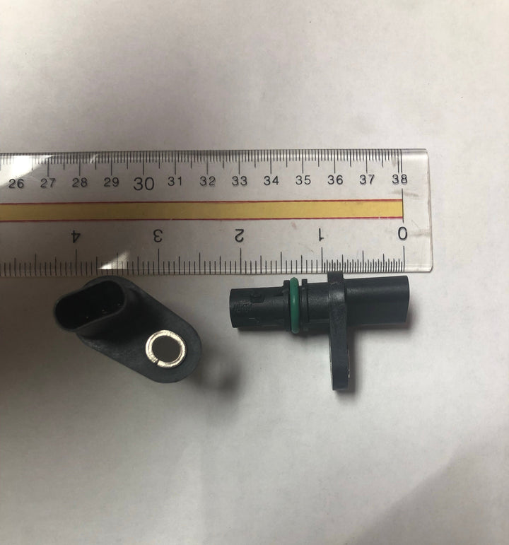 Advance Truck Parts USA studio perspective displaying two heavy-duty camshaft and crankshaft position sensors next to a measurement ruler, highlighting the 3-prong oval connector and the side profile with a green o-ring for scale