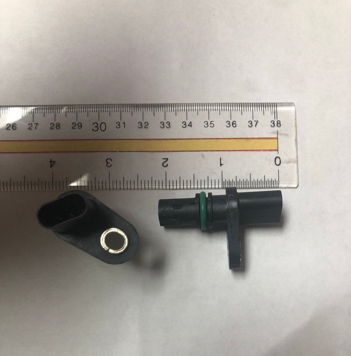Advance Truck Parts USA branded studio perspective displaying two heavy-duty camshaft and crankshaft position sensors next to a measurement ruler, highlighting the 3-prong oval connector and the side profile with a green o-ring for scale